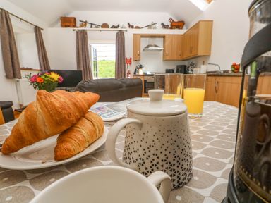 A kitchen and dining area with croissants on a plate juice glasses and a teapot on a table at The Coach House in Hayle
