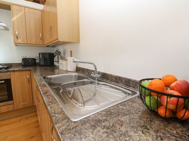 A kitchen countertop with a sink a fruit basket and wooden cabinets at The Coach House in Hayle
