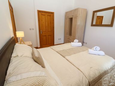 A bedroom with a bed with rolled towels a wooden wardrobe a bedside table with a lamp and a wall mirror at The Coach House in Hayle