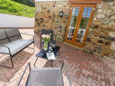 An outdoor patio with metal chairs a table with flowers wine and glasses near wooden double doors and a stone wall at The Coach House in Hayle