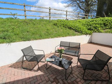 An outdoor patio area with black mesh chairs a small table with a bottle wine glasses and flowers at The Coach House in Hayle