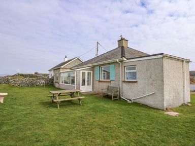 A house with a wooden picnic table and bench on a lawn at Tegawelon in Llandanwg near Harlech