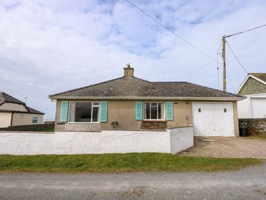 A single-story house with two windows and a garage door and a low white wall in front at Tegawelon in Llandanwg near Harlech