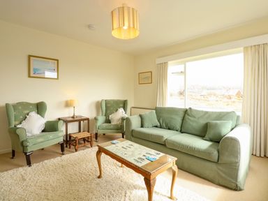 A living room with green sofa and armchairs a wooden coffee table and a small side table with a lamp at Tegawelon in Llandanwg near Harlech