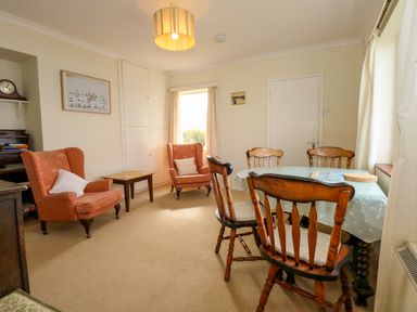 A living room with two armchairs a dining table with chairs and a door at Tegawelon in Llandanwg near Harlech