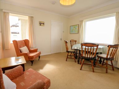 A living room with wooden chairs and a table near a large window and armchairs by a small window at Tegawelon in Llandanwg near Harlech