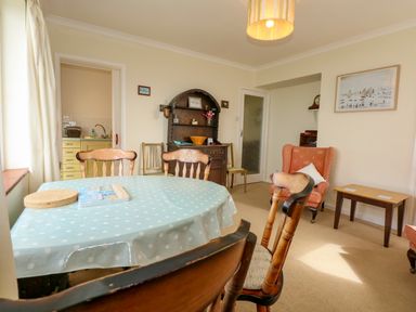 A dining room with a table covered with a polka dot tablecloth surrounded by wooden chairs an armchair and a wooden cabinet at Tegawelon in Llandanwg near Harlech