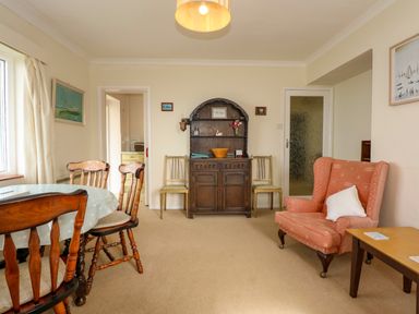 A dining room with wooden chairs a table a cabinet and an armchair at Tegawelon in Llandanwg near Harlech