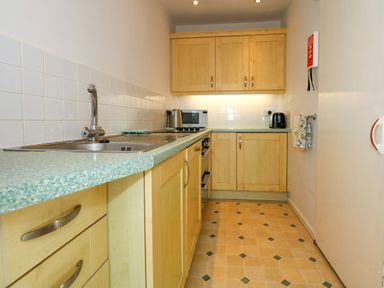 A galley kitchen with wooden cabinets a green speckled countertop a sink a microwave kettle and toaster at Tegawelon in Llandanwg near Harlech