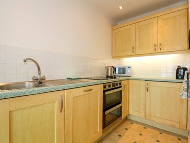 A kitchen with wooden cabinets a sink an oven microwave kettle and toaster at Tegawelon in Llandanwg near Harlech