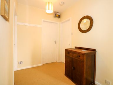 A hallway with two white doors a wooden cabinet and a round mirror on a beige wall at Tegawelon in Llandanwg near Harlech