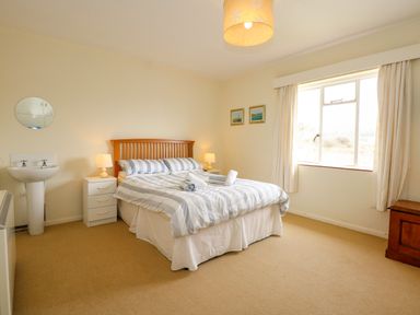 A bedroom with a double bed striped bedding two bedside tables with lamps a sink a window with curtains and two paintings on the wall at Tegawelon in Llandanwg near Harlech