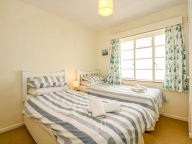 A bedroom with two single beds with striped bedding a window with curtains and a bedside lamp at Tegawelon in Llandanwg near Harlech