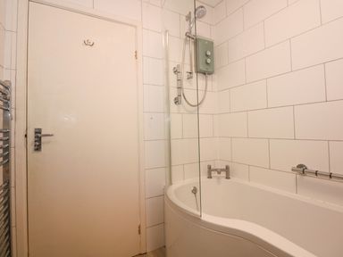 A bathroom with white tiled walls a curved bathtub shower and a closed door at Tegawelon in Llandanwg near Harlech