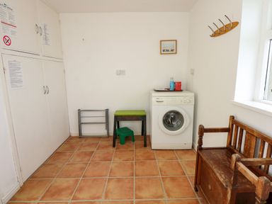 A laundry room with a washing machine wooden bench small stool and wall hooks at Tegawelon in Llandanwg near Harlech