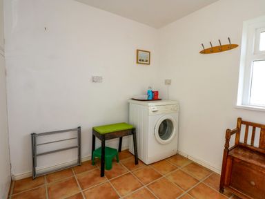 A laundry room with a washing machine wooden bench and wall hooks at Tegawelon in Llandanwg near Harlech