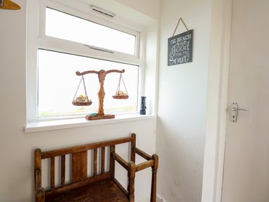 A wooden bench under a window with a wooden balance scale and a small sign on the wall at Tegawelon in Llandanwg near Harlech
