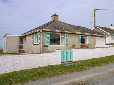 A small house with a tiled roof turquoise window shutters and a turquoise gate in front of a white wall at Tegawelon in Llandanwg near Harlech