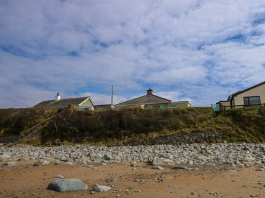 A rocky beach with houses on a grassy hill under a cloudy sky at Tegawelon in Llandanwg near Harlech
