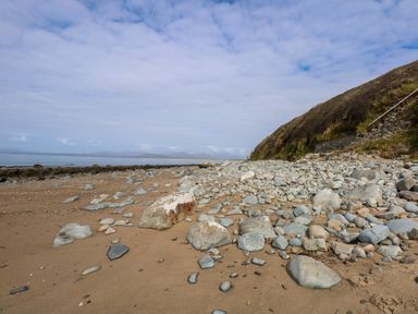 A beach with sand and scattered stones next to a hill with stairs leading down to the shore at Tegawelon in Llandanwg near Harlech