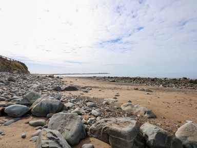 A sandy and rocky beach with a section of a wooden fence on a grassy slope at Tegawelon in Llandanwg near Harlech