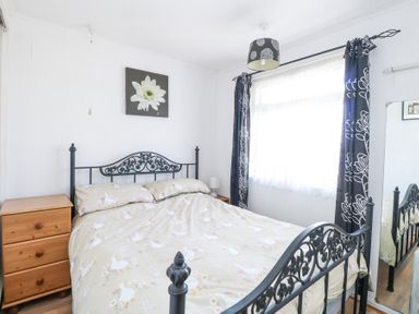 A bedroom with a metal bed frame a wooden dresser a window with curtains and a floral painting above the bed at Chalet 21 in Newport Norfolk
