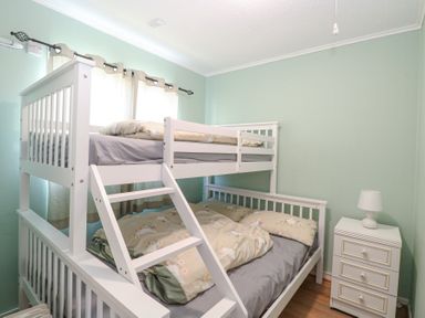 A bedroom with a white bunk bed a nightstand with a lamp and curtains on the window at Chalet 21 Newport Norfolk