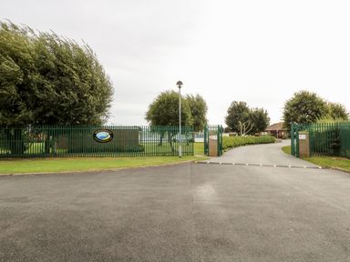 A gated entrance with a green fence and trees lining a curved driveway at Sundowner in Newport Norfolk
