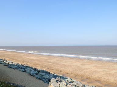 A sandy beach with rocks along the shore and calm sea under a clear sky at Chalet 21 in Newport Norfolk