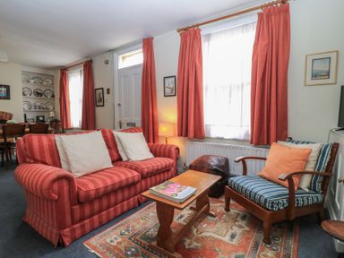 A sitting room with a red striped sofa, a wooden armchair with blue striped cushions, a wooden coffee table, and red curtains at The Townhouse in Salisbury