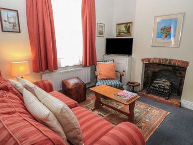 A living room with a striped red sofa cushions a wooden coffee table an armchair a small TV and a brick fireplace at The Townhouse in Salisbury