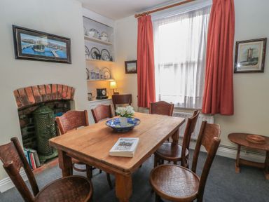 A dining room with wooden table and six chairs a fireplace with brick surround shelves with plates and a window with red curtains at The Townhouse in Salisbury