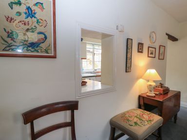 A small seating area with a chair wooden side table and lamp next to a window opening showing a kitchen at The Townhouse in Salisbury