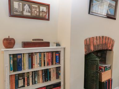 A bookshelf filled with books next to a small fireplace with a green stove and a brick arch at The Townhouse in Salisbury