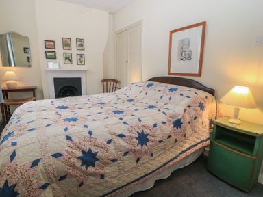 A bedroom with a bed covered by a patterned quilt two lamps on bedside tables a fireplace and framed pictures on the wall at The Townhouse in Salisbury