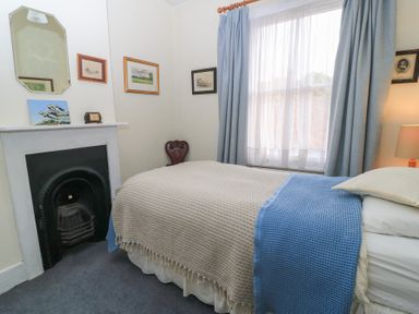 A bedroom with a bed next to a window with curtains and a fireplace with pictures on the wall at The Townhouse in Salisbury