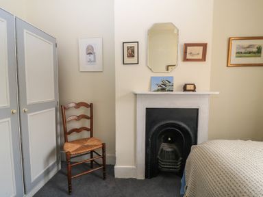 A bedroom corner with a wooden chair next to a closet and a fireplace with a mirror and pictures above it at The Townhouse in Salisbury