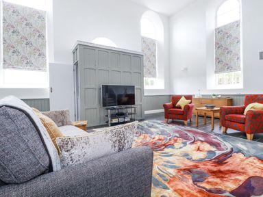 A sitting room with a gray sofa red armchairs a colorful rug and a television at Trelowth Chapel in Polgooth