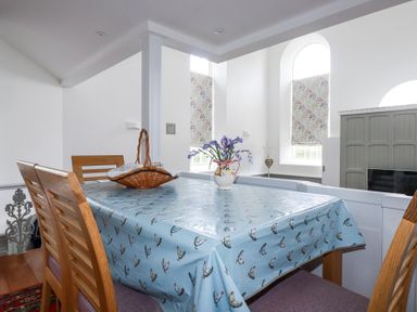 A dining room with wooden chairs a table with a blue tablecloth a basket and a vase of flowers at Trelowth Chapel in Polgooth