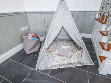 A corner with a small gray teepee tent on a tiled floor with a basket of toys and stairs nearby at Trelowth Chapel in Polgooth