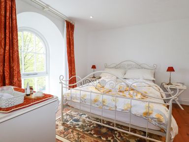 A bedroom with a metal bed frame floral bedding and red curtains at Trelowth Chapel in Polgooth