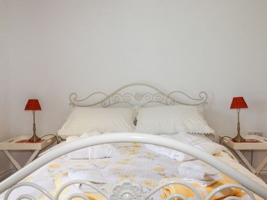 A bedroom with a white metal bed frame white pillows and side tables with red lamps at Trelowth Chapel in Polgooth