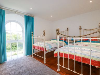 A bedroom with two beds a large arched window with blue curtains and carpeted floor at Trelowth Chapel in Polgooth