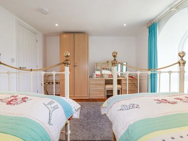 A bedroom with two beds a wooden wardrobe a dressing table with a mirror and a blue curtain at Trelowth Chapel in Polgooth