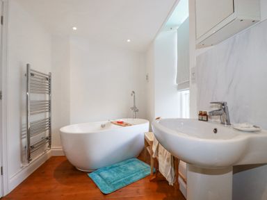 A bathroom with a freestanding bathtub a sink a towel rack and a wooden floor at Trelowth Chapel in Polgooth