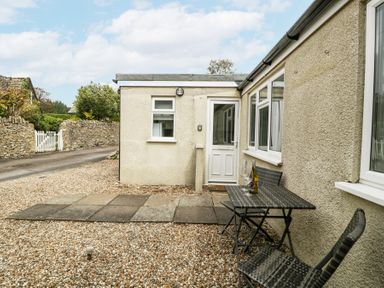 A patio area with a table and two chairs outside a cream-colored house at Spring Cottage in Birdlip near Brockworth