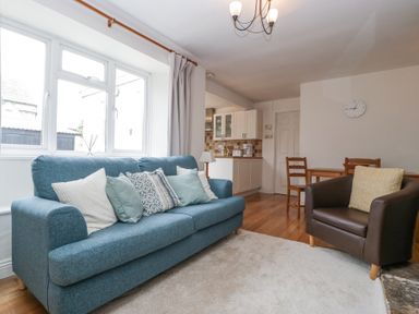 A living room with a blue sofa and pillows a brown armchair a dining table with chairs and a kitchen area at Spring Cottage in Birdlip near Brockworth