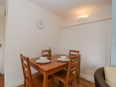 A dining area with a wooden table and four chairs set with plates bowls wine glasses and a wine bottle at Spring Cottage in Birdlip near Brockworth