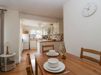 A kitchen and dining area with wooden table set for two and white cabinets at Spring Cottage in Birdlip near Brockworth