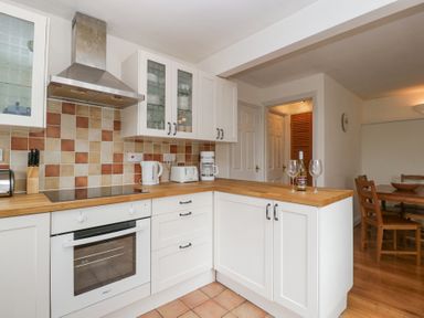 A kitchen with white cabinets wooden countertop tiled backsplash and dining table with chairs at Spring Cottage in Birdlip near Brockworth